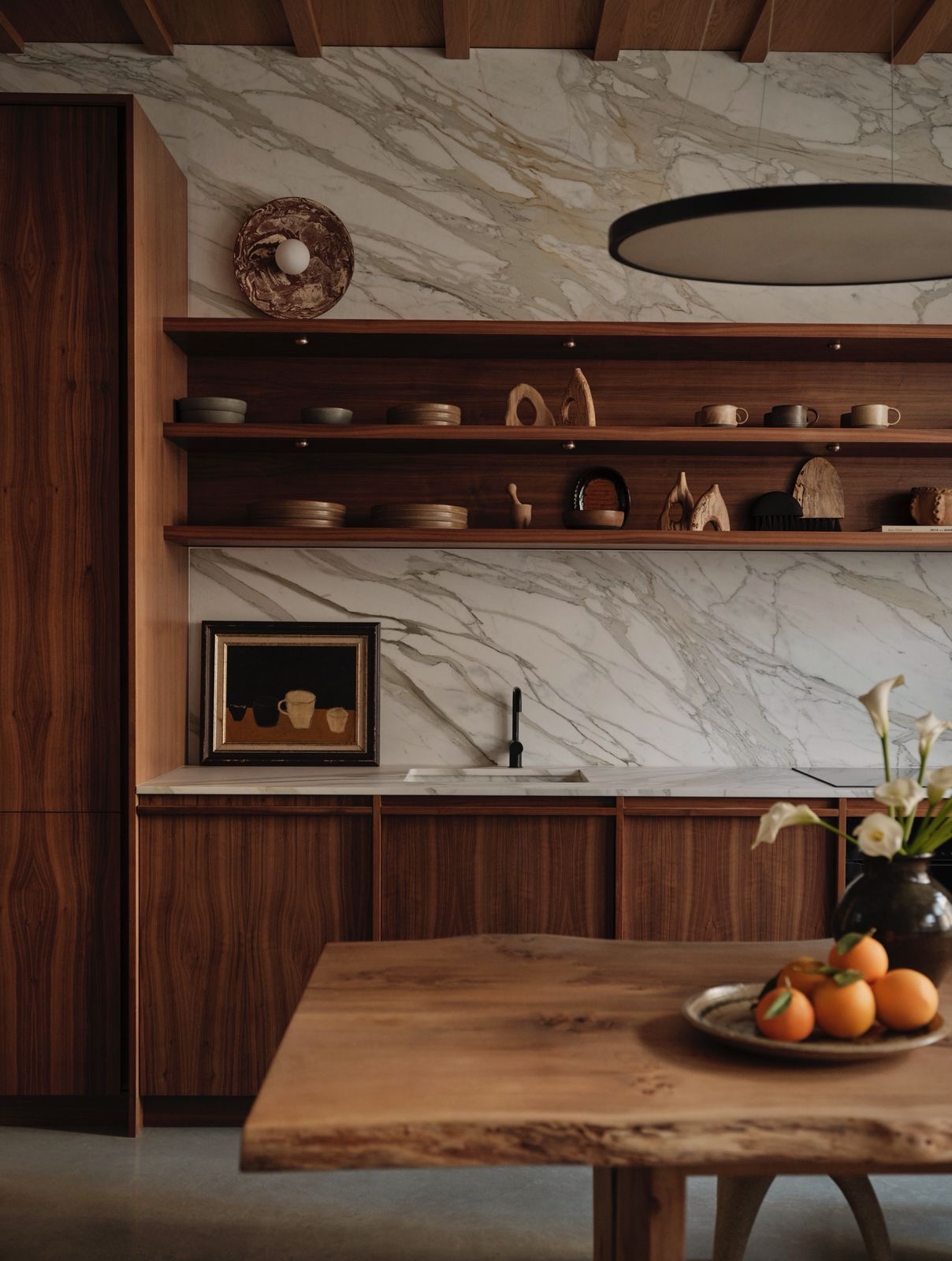 A walnut kitchen with a marble splashback, handmade ceramics and a bowl of oranges